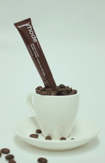 A skincare tube in a coffee cup filled with coffee beans on a saucer.