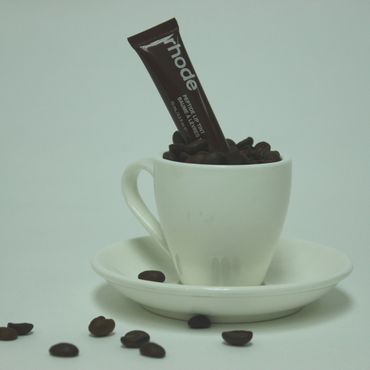 White coffee cup filled with coffee beans and a Rhodi product tube inside.