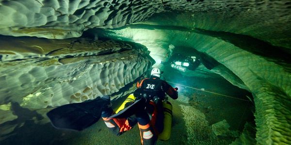Sidemount cave diver following a guideline through a cave passage