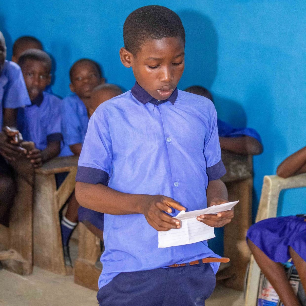 A boy reading from a paper in a classroom.