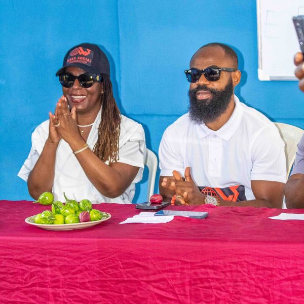 Two people smiling and clapping at a table with a plate of green and red vegetables.