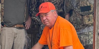 Man in bright orange hunting gear with others in camouflage.