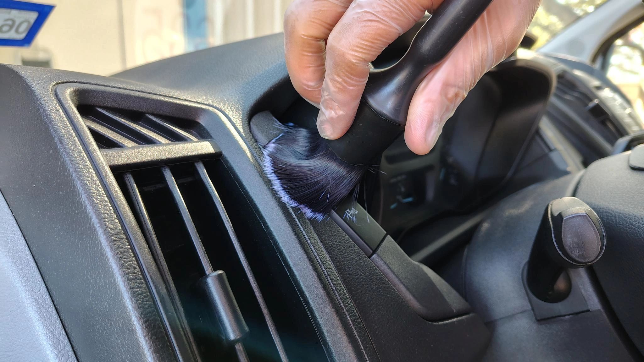 Gloved hand dusting car dashboard with a brush.