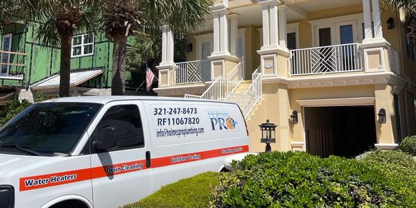 Holmes Pro Plumbing van parked in front of a tropical-style house with palm trees.