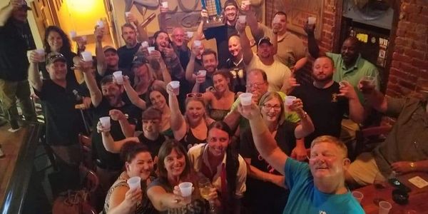 A large group of people raising drinks in a lively bar celebration.