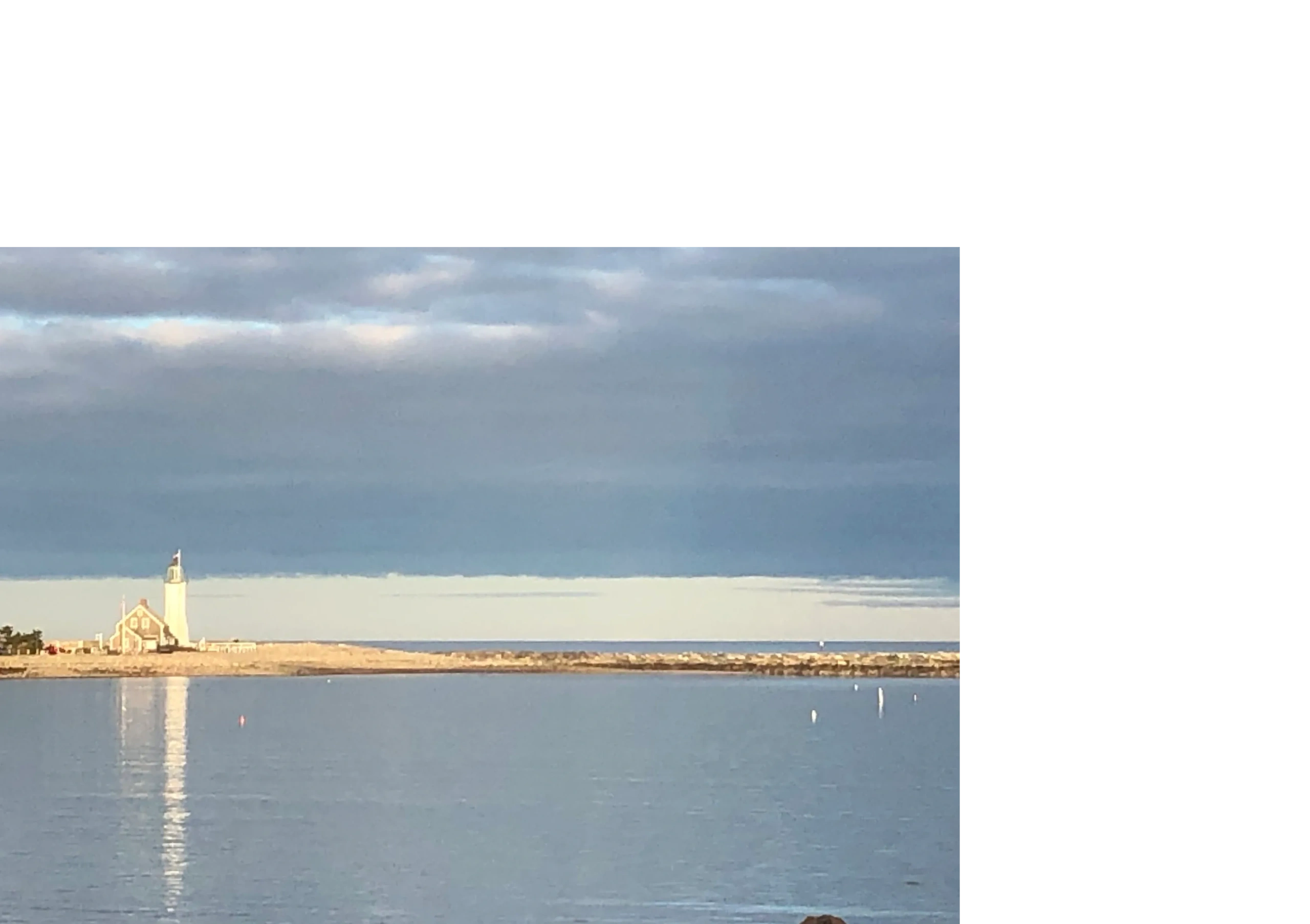 Lighthouse on a calm coastline with cloudy sky.