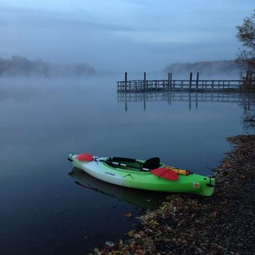 A green kayak rests on the shore of a misty lake at dawn.