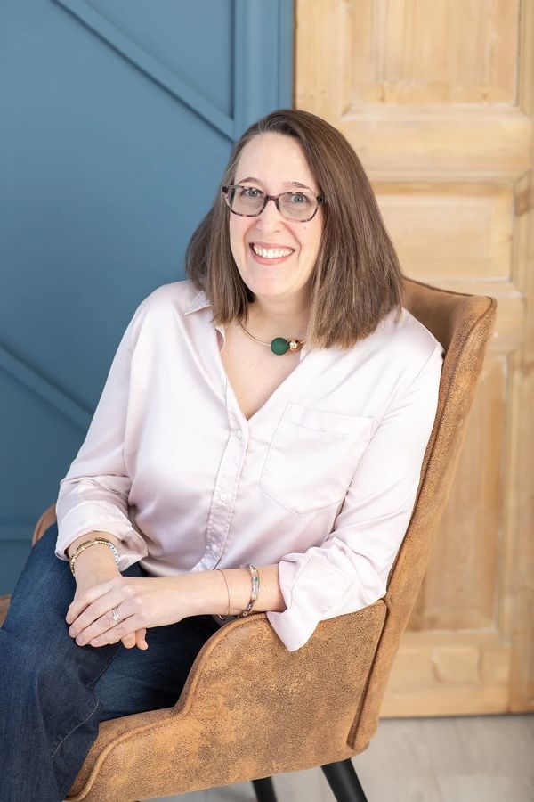 Photo of Author Erica Colahan sitting in a chair and smiling.
