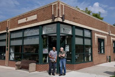 Two men standing outside a corner brick building.