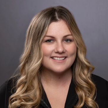 Young woman with long blonde wavy hair smiling against a gray background.