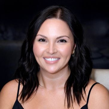 Smiling woman with dark hair in a black top against a dark background.