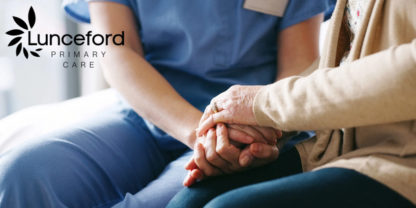 A medical provider in blue scrubs holds hands with an older patient, conveying warmth and compassion during a discussion about the patient's health