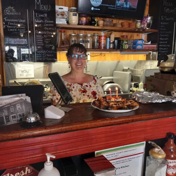 Naomi standing behind the service counter, in front of the menu board, smiling