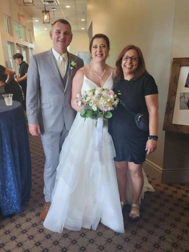 Bride and groom with a woman in a black dress at a wedding.