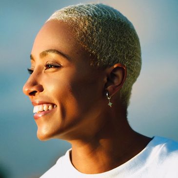 Smiling person with short blond hair wearing a white Adidas shirt.