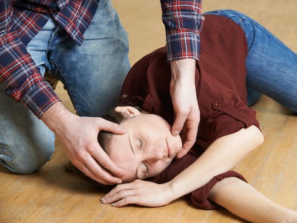 Person assisting an unconscious woman on the floor.