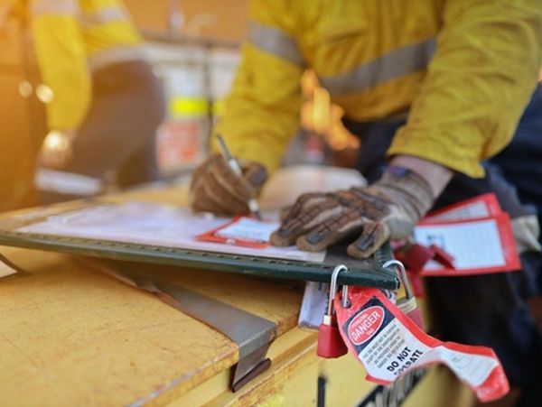 Worker in safety gloves filling out a form with danger tag on clipboard.