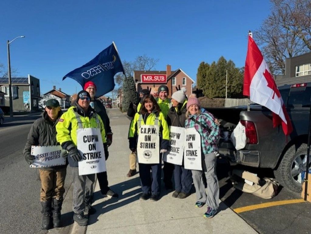 Group of postal workers on strike holding signs and flags outdoors.
