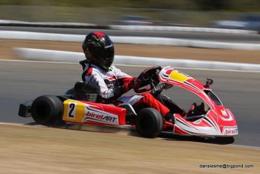 A go-kart racer in red and white gear speeding on a track.