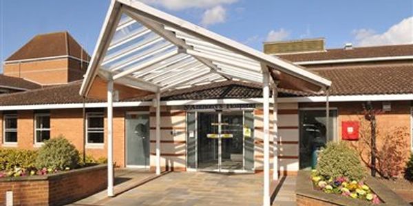 Entrance to a modern building with a glass canopy and brick walls.
