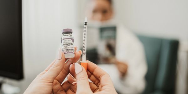 Hands holding a drug vial and syringe with a blurred person in background.