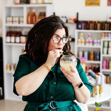 Woman tasting a drink in a store with shelves of products behind her.