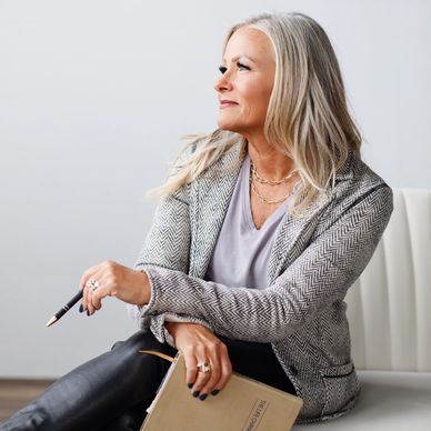 Confident mature woman holding a pen and notebook, looking thoughtfully to the side.