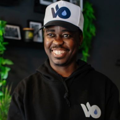 Smiling man wearing a black hoodie and white cap with a 'VO' logo.