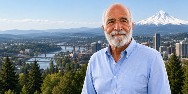 Older man with beard standing in front of city and mountain.