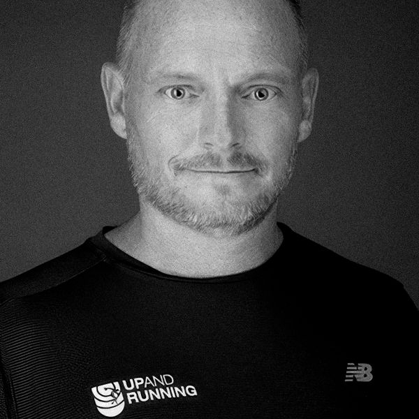 Black-and-white portrait of a chiropractor in Dubai wearing a sports shirt with logos.