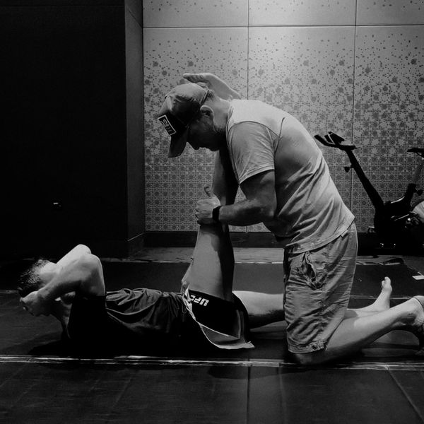 A trainer assists an athlete with a leg stretch on the floor in a gym.