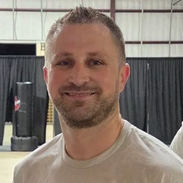 Smiling man in a light gray shirt indoors.