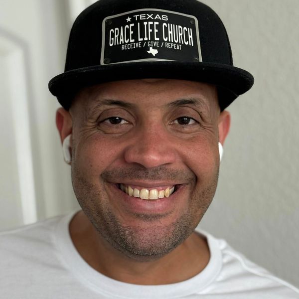 Smiling man wearing a Texas Grace Life Church cap and white shirt.