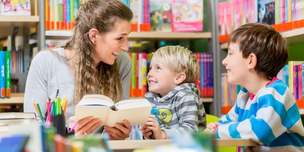 A mother smiling at two young sons, holding an open book.