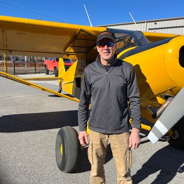 Man standing next to a yellow small airplane outdoors.