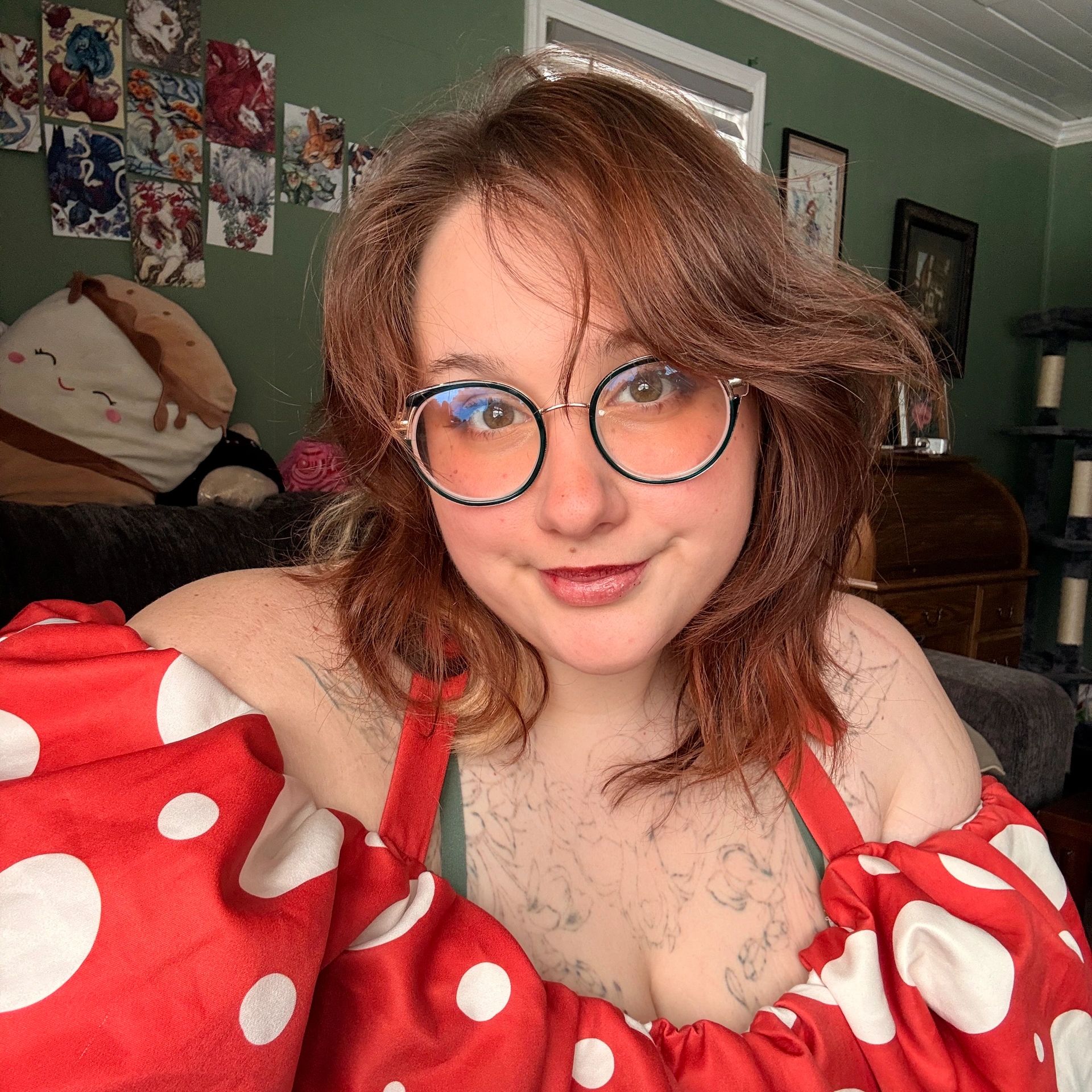 Person with round glasses and red polka-dot top smiling indoors.