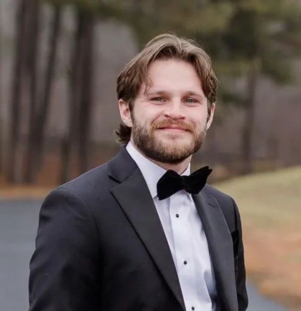 Smiling man in a tuxedo with a bow tie outdoors.