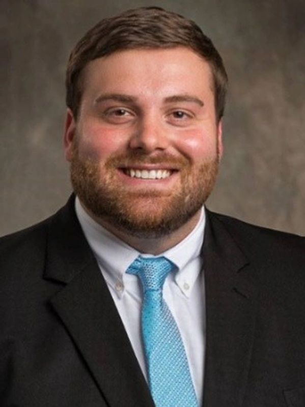 Smiling man in a black suit and blue tie.