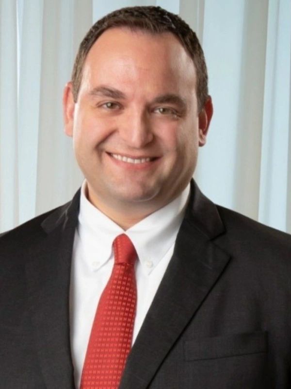 Smiling man in a black suit with a red tie and white shirt.
