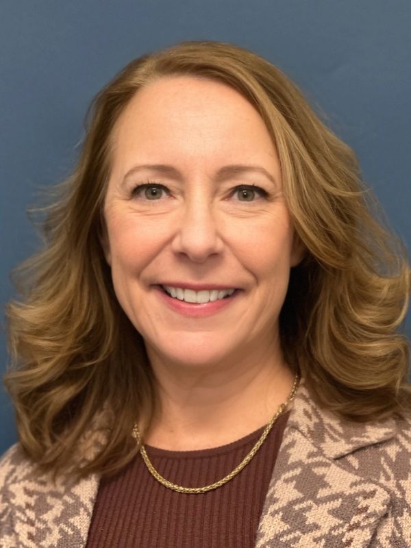 Smiling woman with wavy hair in patterned blazer.