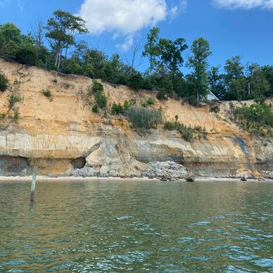 Eroded cliffside with trees and water in front under a blue sky.