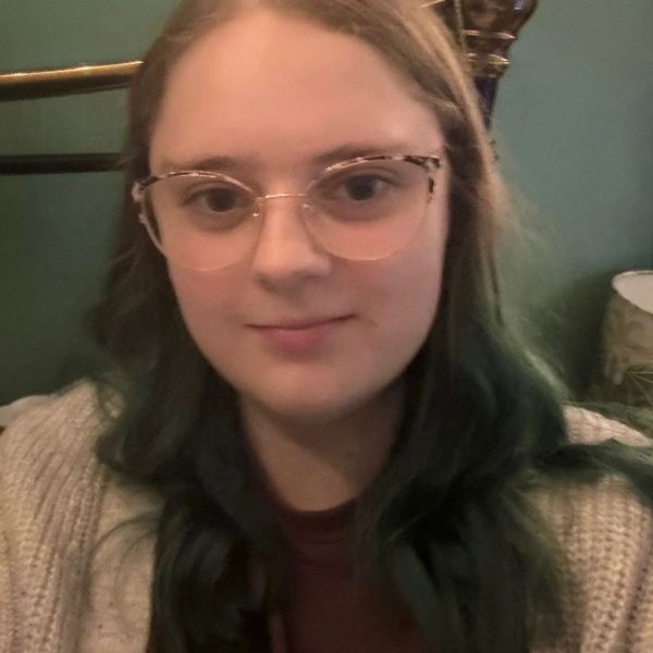Young woman with glasses and long hair smiling gently.