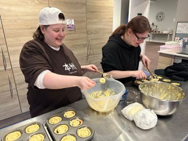 Two people happily preparing muffins in a kitchen.