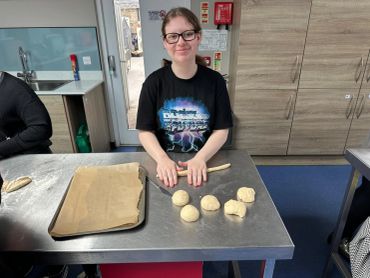 A young person rolling dough balls on a kitchen table, smiling.