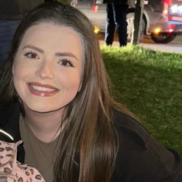 A young woman smiling outdoors at night with grass and a parked car in the background.