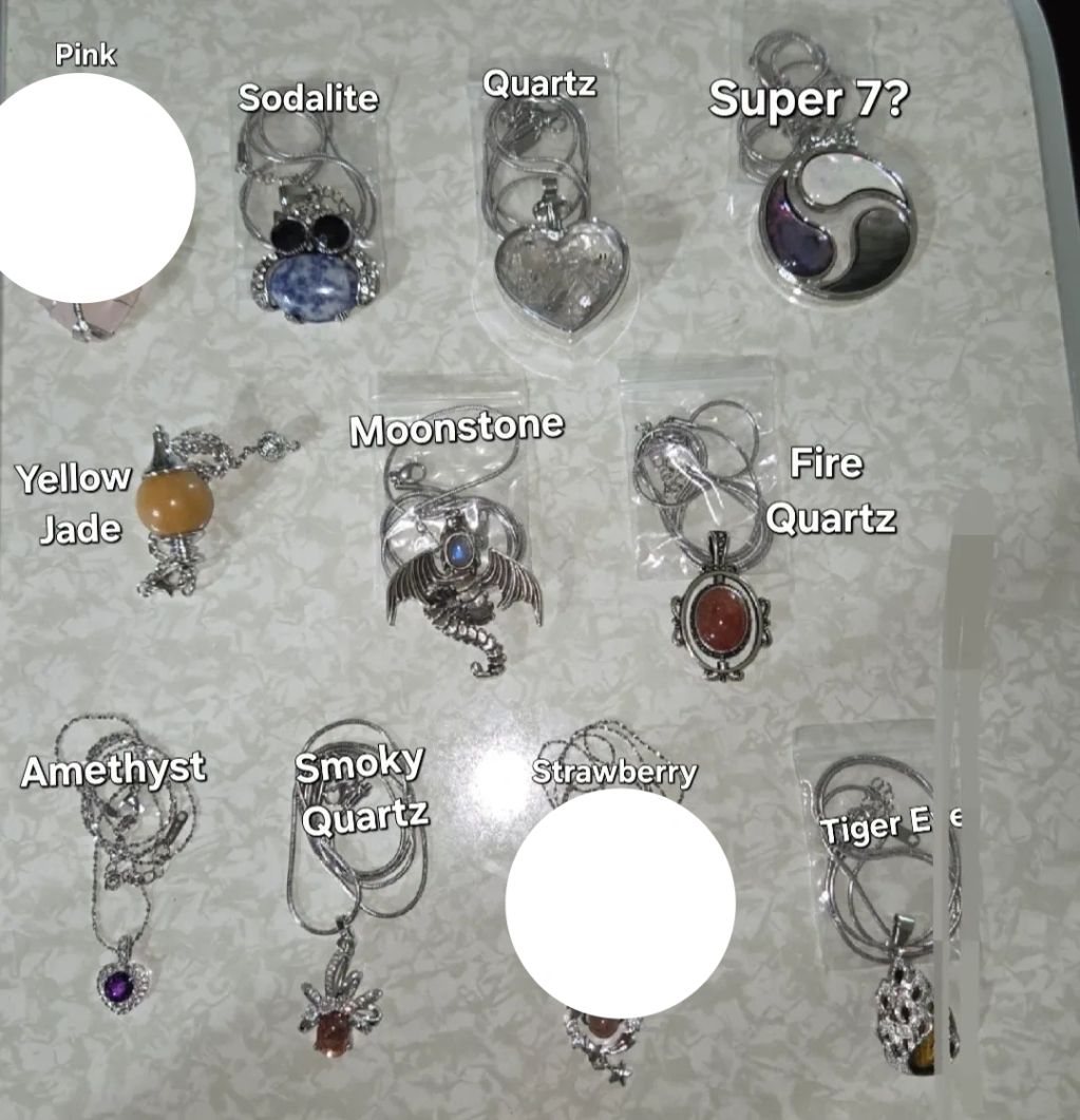 Various crystal necklaces labeled by type and color on a table.