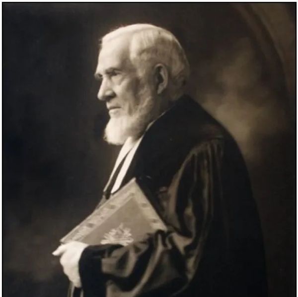 An elderly man in robe holding a book.