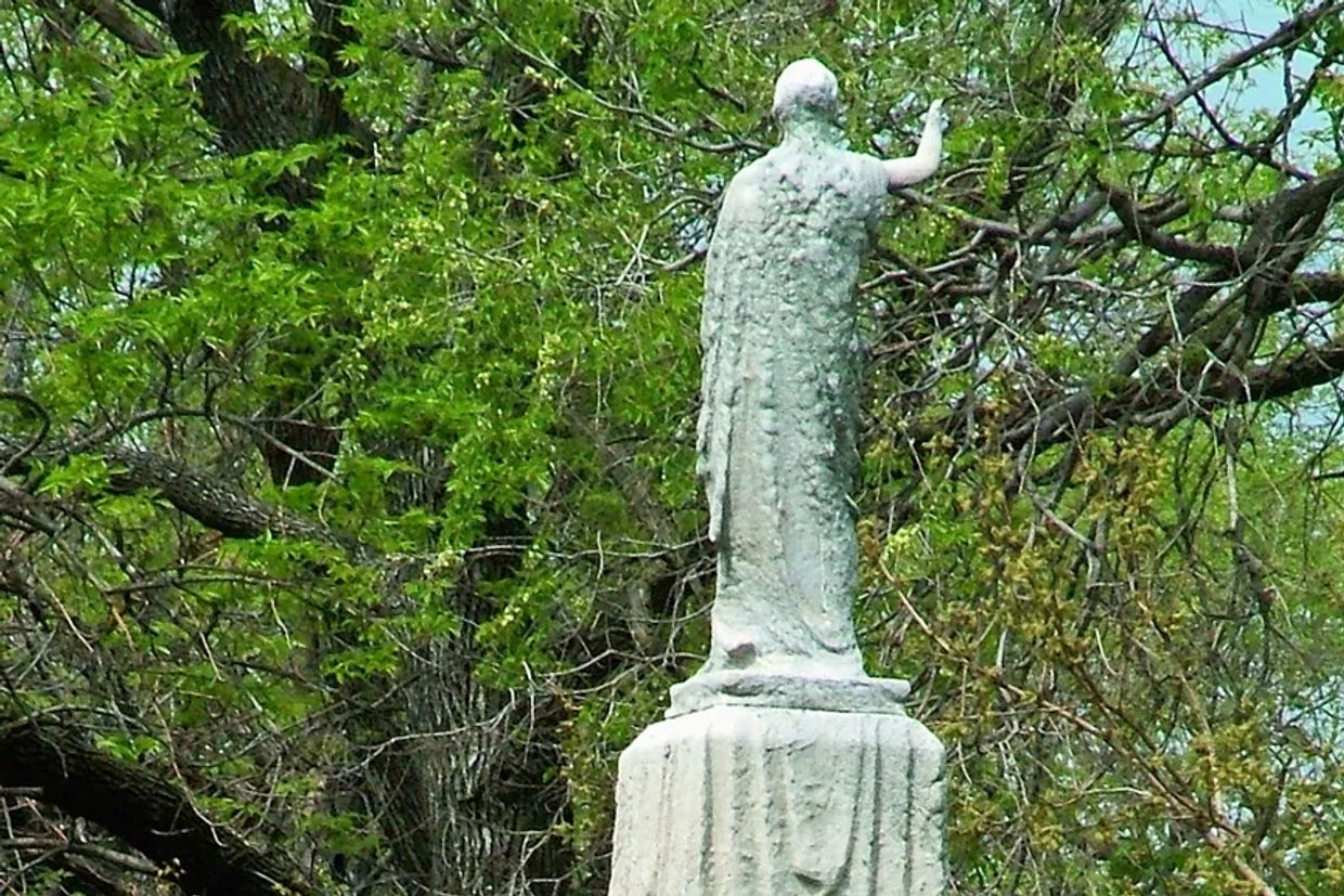 Rear view of a weathered statue surrounded by green trees.