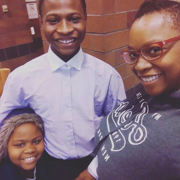 Three smiling individuals posing indoors against a brick wall.