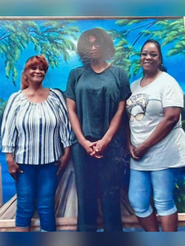 Three women standing in front of a scenic blue mural with greenery.